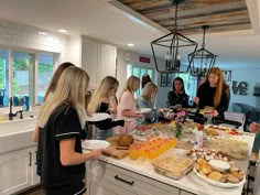 a group of women standing around a kitchen counter with food on it's trays