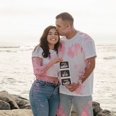 a man and woman standing next to each other on the beach with pink paint all over them