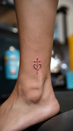 a small cross and heart tattoo on the side of someone's foot, which is also in black ink