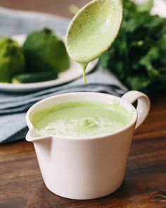 a spoon full of broccoli soup is being held up by a white bowl