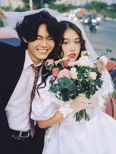 a bride and groom posing for a photo in front of a car on their wedding day