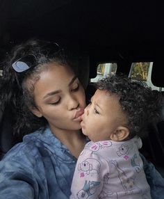 a woman kissing a small child in the back seat of a car with her eyes closed