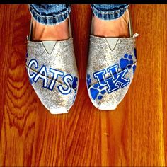 someone's shoes with the word cats painted on them are sitting on a wooden floor