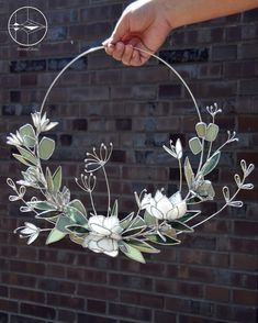 a hand holding a metal hoop with white flowers and leaves on it, in front of a brick wall