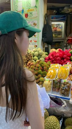 a woman wearing a green hat standing in front of a display of fruit at a market