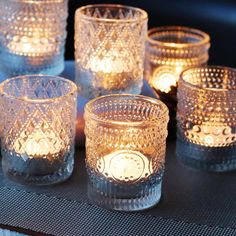 many lit candles are sitting on a table with some glass cups in front of them