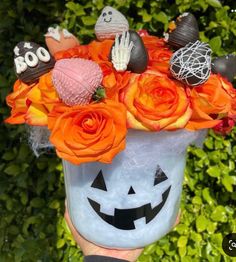 a person holding up a halloween bucket with pumpkins and other decorations on it's face