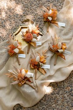 four boutonnieres with orange and white flowers are on a cloth covered table