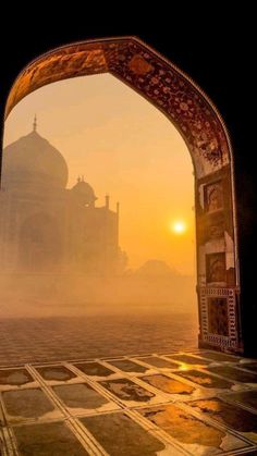 the sun is setting in front of an arch with a view of a taj mahal