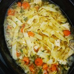 a crock pot filled with chicken noodle soup and carrots on the side