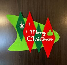 a merry christmas sign hanging on the side of a wooden door with green and red pennants