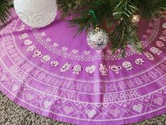 an ornament hanging from a christmas tree on a purple tablecloth next to a white teddy bear