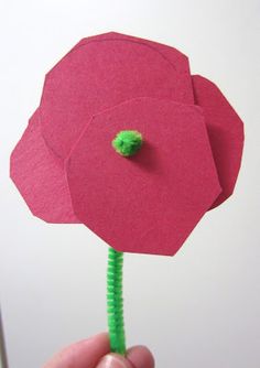 a hand holding a paper flower with a green thread in it's center and the petals are red