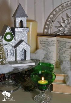 a green glass candle holder sitting on top of a table next to an open book