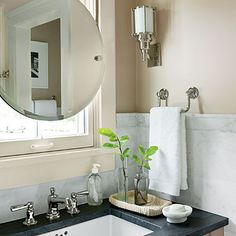 a bathroom sink sitting under a mirror next to a window with a potted plant in it