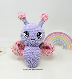 a small crocheted toy sitting on top of a white table next to a rainbow