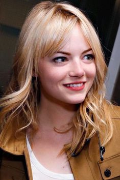 a woman with blonde hair is smiling for the camera while wearing a tan jacket and white t - shirt