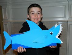 a young boy holding up a paper cut out of a blue shark with sharp teeth