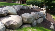 a pile of rocks sitting on top of a lush green hillside next to a house