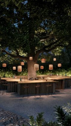 an outdoor dining area is lit up at night with paper lanterns hanging from the tree