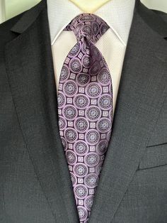 This 100% woven silk tie has a gorgeous weight and thickness to the finish. With woven medallions in shades of purple and black, this is a necktie that makes a statement. To be worn with shirts in white, blue, pink, beige and grey. This tie also pairs well with shirts with small plaids and mini checks. See the sister color in blue. Formal Purple Neckwear With Ties, Elegant Purple Neckwear For Black Tie Event, Formal Purple Standard Tie, Classic Lavender Tie For Business, Classic Purple Neckwear For Formal Occasions, Purple Suit And Tie Accessories For Black Tie Events, Elegant Purple Tie For Office, Elegant Purple Office Ties, Pink Beige