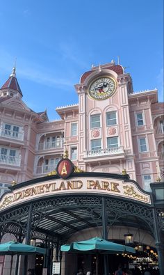 the entrance to disneyland land park with people walking around it and a clock tower in the background