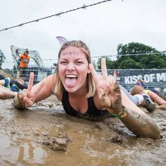 a woman laying on the ground in mud with her hands up and two people behind her making peace signs