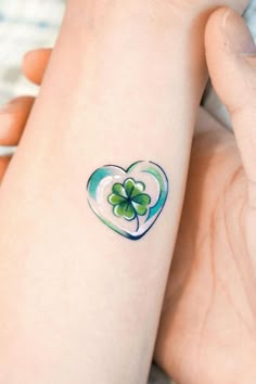 a woman's arm with a shamrock heart tattoo on her left wrist, and a four leaf clover in the shape of a heart