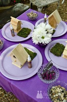 purple table cloth with birdhouses and flowers on it, surrounded by small bowls filled with rocks