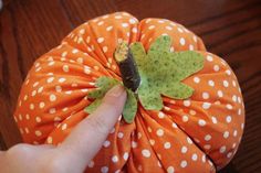 a hand is pointing at an orange pumpkin with white polka dots on it and a green leaf sticking out of the top