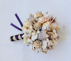 a bridal bouquet made up of seashells and purple ribbon on a white table