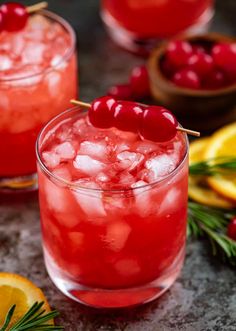 two glasses filled with cranberry punch and garnished with orange slices, rosemary, and cherries