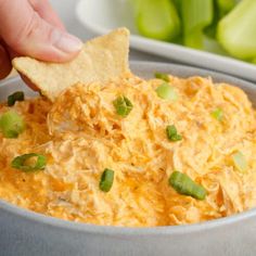 a hand dipping a tortilla chip into a bowl of dip