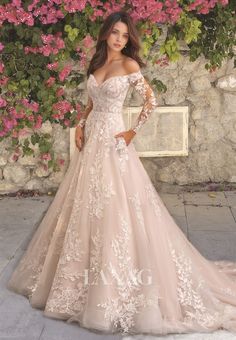 a woman in a wedding dress posing for the camera with pink flowers on her wall behind her