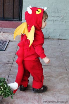 a little boy in a red dragon costume standing next to a potted plant and looking at the ground