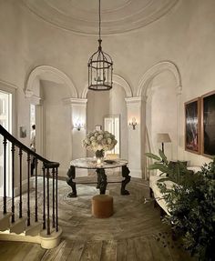 an elegant foyer with chandelier and marble table surrounded by greenery in the center