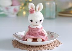 a crocheted bunny doll sitting in a bowl on a doily place mat