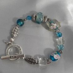 This 8" Bracelet Has A Cute Toggle Closure That Says "Peace Begins With A Smile". It Has Clear And Teal Glass Beads, Metal Beads, A Sterling Silver .925 Murano Bead And Two Lampwork Beads Adorned With Flowers In Teal And Pink. A Very Unique Bracelet That Would Make A Great Gift For Someone In Your Family, Your Mom, Grandmother, Sister Or Favorite Aunt Or Maybe Your Bestie! Blue Beaded Bracelets For Spring Gift, Spring Turquoise Bracelet Gift, Turquoise Bracelet Spring Gift, Spring Gift Turquoise Bracelet, Blue Beaded Bracelets As Spring Gift, Bohemian Blue Beaded Bracelets For Spring, Blue Round Beads Bracelet For Spring, Handmade Blue Beaded Bracelets For Spring, Handmade Turquoise Beaded Bracelets For Spring