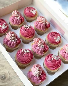 cupcakes with pink frosting and bows in a white box on a table