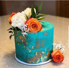 a blue cake with orange and white flowers on it sitting on top of a table