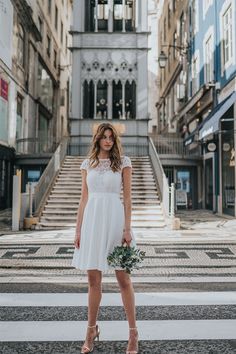 a woman is standing in front of some stairs holding a bouquet and looking at the camera