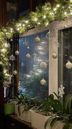 christmas decorations are hanging from the window sill in front of a green potted plant