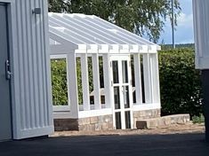 a small white building with a door and windows on the side of it in front of some bushes