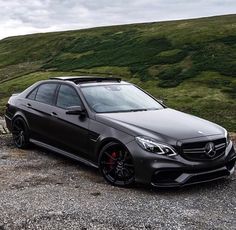 a black car parked on the side of a road in front of a hill with green grass