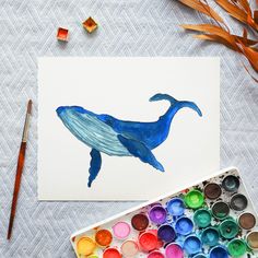 a blue whale painted on white paper next to watercolors