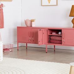 a pink cabinet in the corner of a room next to a white rug and lamp