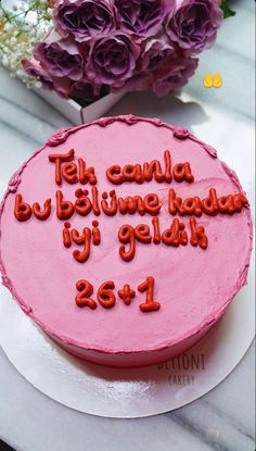 a pink cake sitting on top of a white plate next to purple and red flowers