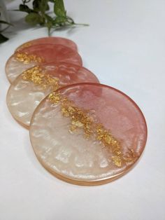 three pink and gold coasters sitting on top of a white table next to a plant