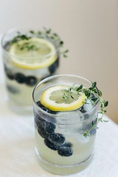 two glasses filled with blueberries and lemonade on top of a white tablecloth