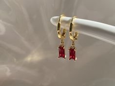 Ruby red dangly hoop earrings Gold plated brass hoop earrings Hoop size approximately 13mm Ruby red cubic zirconia charm size approximately 8mm x 4mm Every item comes in our frosted travel pouch  Gift wrap pouch & box set available, also sold separately Gold And Red Earrings Dangle, Ruby Earrings Aesthetic, Jewelry For Red Dress Formal, Red Dangly Earrings, Red Gem Earrings, Red Prom Dress Gold Jewelry, Gold And Ruby Earrings, Red Dress Accessories Jewelry Formal, Ruby Hoop Earrings